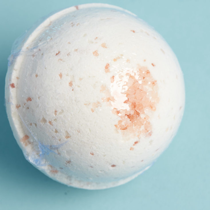 closeup on peach sprinkles on the top of a white bath bomb in plastic wrap