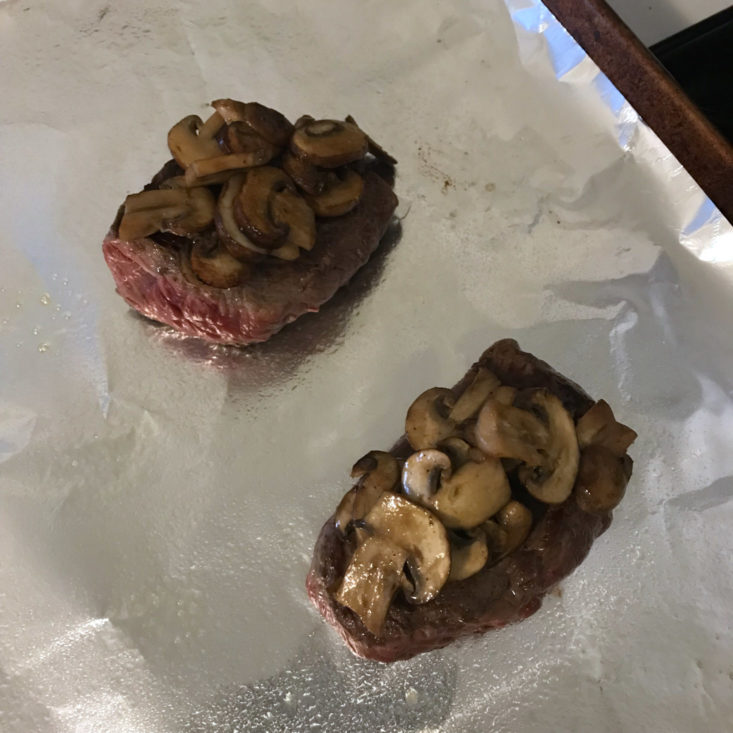 steaks topped with mushrooms on baking sheet