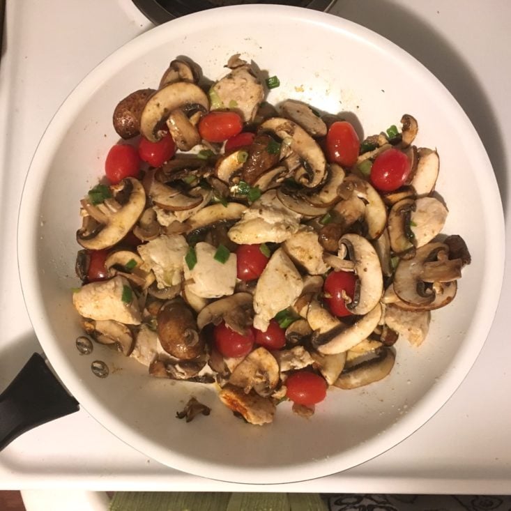 mushrooms, tomatoes, chicken, and green onions cooking in a large, white skillet for the cajun grits recipe